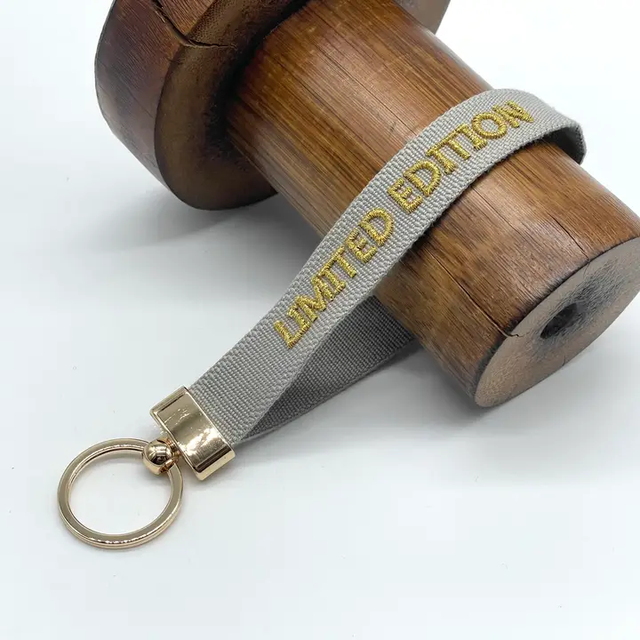 Schlüsselanhänger Limited Edition – hellgraues Band mit goldener Stickerei und goldenem Ring
